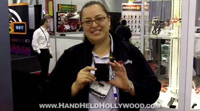 A woman holding up a cell phone at a trade show, showcasing the latest Quikswipe technology.