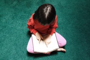 A little girl reading a book on the floor.