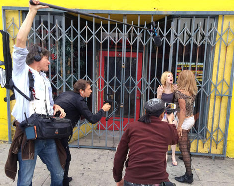 Several individuals, participating in a free workshop at the Santa Monica Apple Store on iPhone filmmaking, appear to be filming or photographing a woman standing behind a metal gate.
