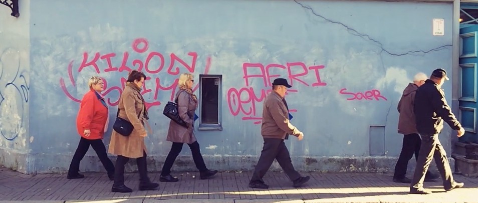 Five adults walking in a line past a wall with graffiti, captured on an iPhone 5S at 120fps by Philip Bloom.