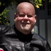 A man smiling while wearing a black leather jacket outdoors.