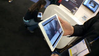 Person holding an iPad displaying an image with another individual sitting in the background.