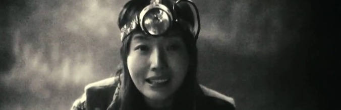 A smiling woman wearing aviator goggles and a headscarf in a Park Chan-Wook film.