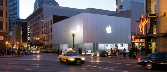 A San Francisco Apple Store with a glowing logo at twilight, as traffic passes by on Friday night.